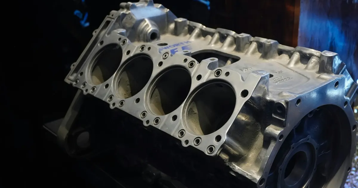 Machined metal engine block with four cylinder bores on a table, an example of automotive CNC parts