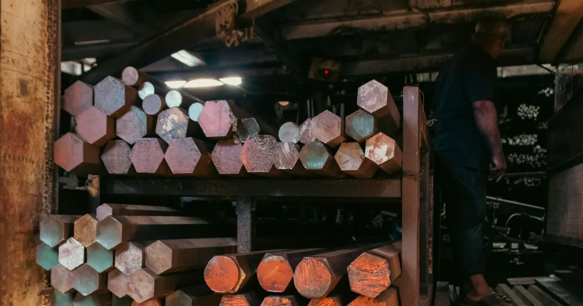 Hexagonal and round metal bars stored on racks in a stock room, relevant to material grade equivalents for machined parts