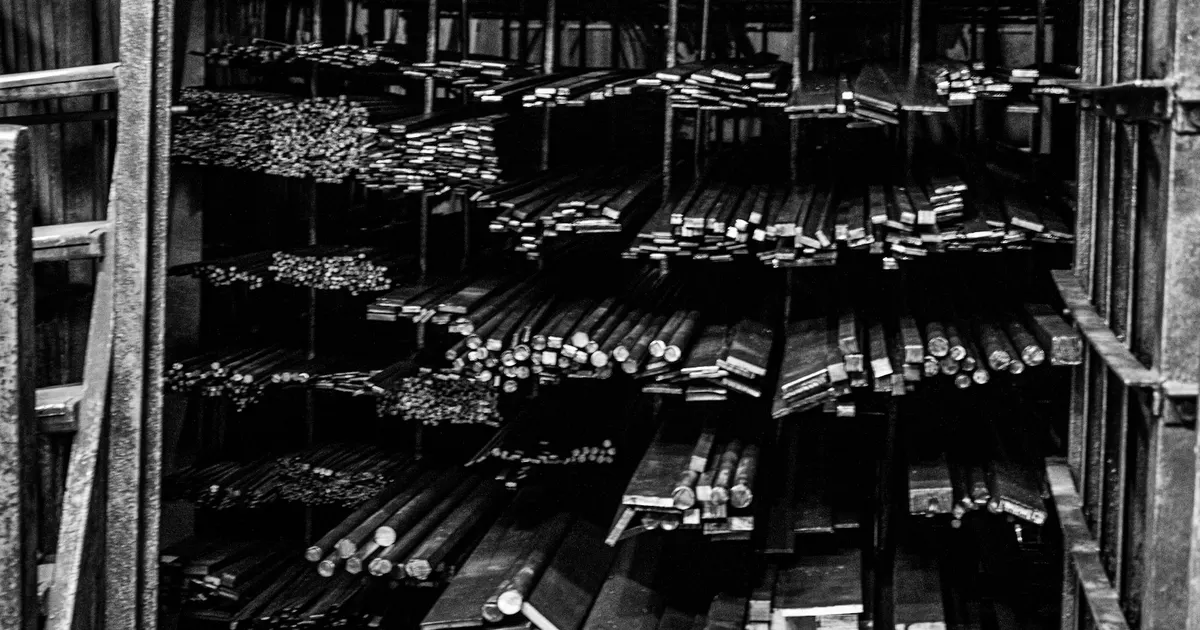 Metal bars of different sizes stacked on shelves in a warehouse, stock covered by a mill test certificate